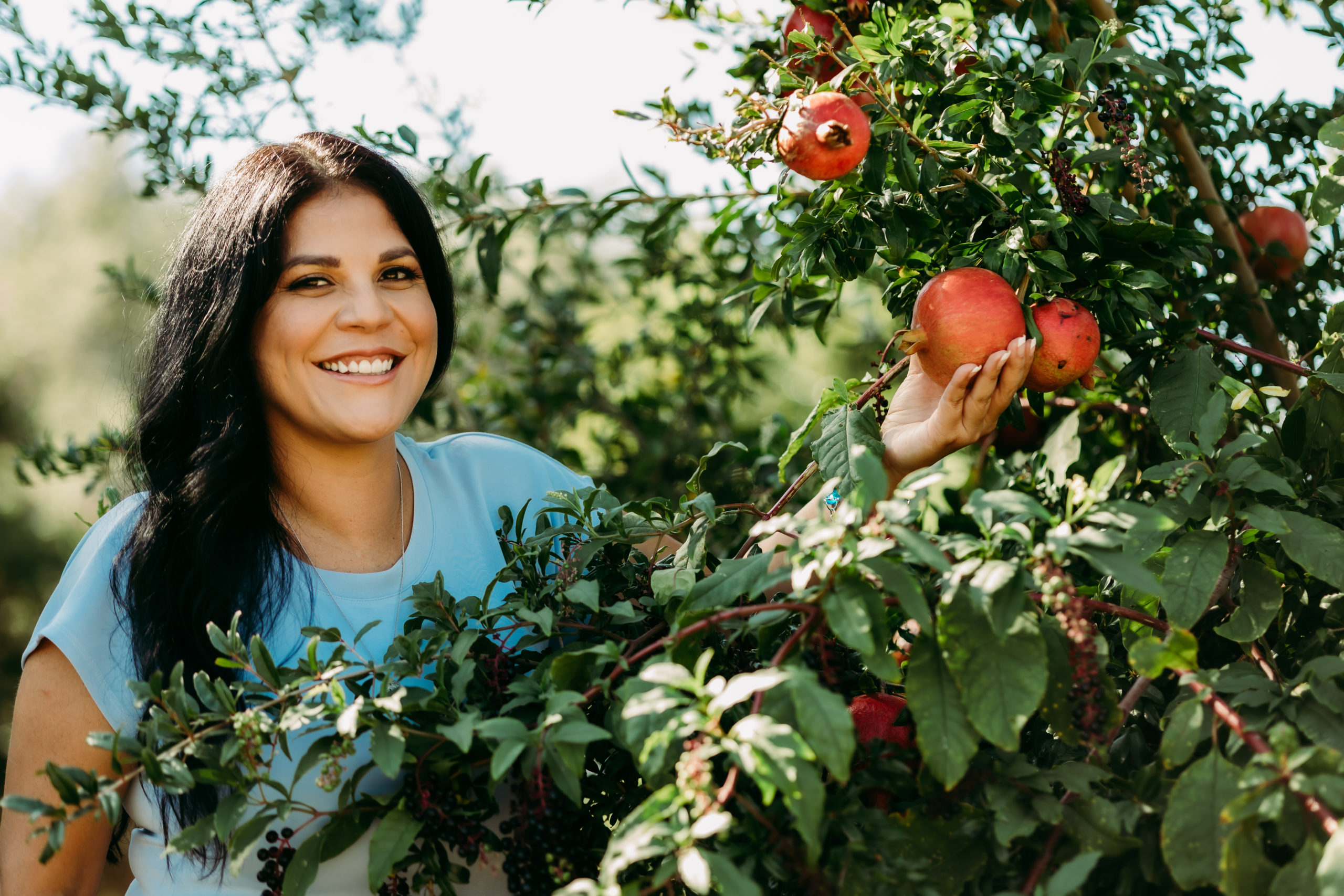 Margesella smiling while picking a pomegranate, symbolizing vibrant health through functional wellness and lifestyle healing